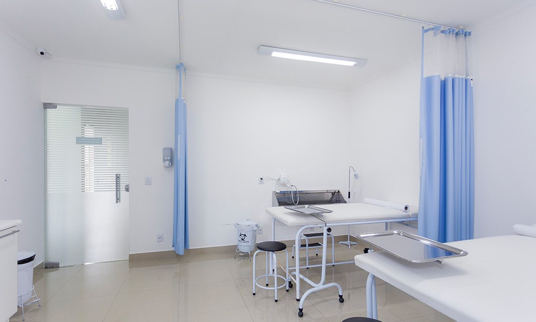 Sala de tratamento de feridas do acervo OMNA, com leitos e cortinas azuis, sem pessoas.